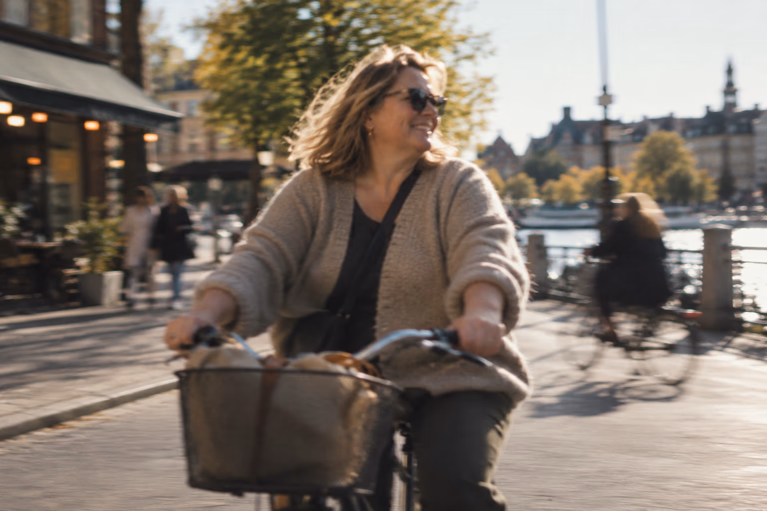 Kvinna i medelåldern cyklar längs ett soligt kajstråk i Stockholm.
