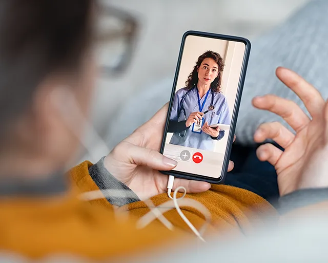 Person holding a smartphone on a video call with a female doctor in medical scrubs.