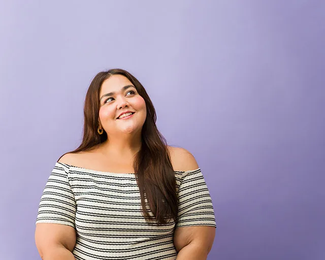 Smiling woman with long brown hair and an off-shoulder striped top against a purple background.